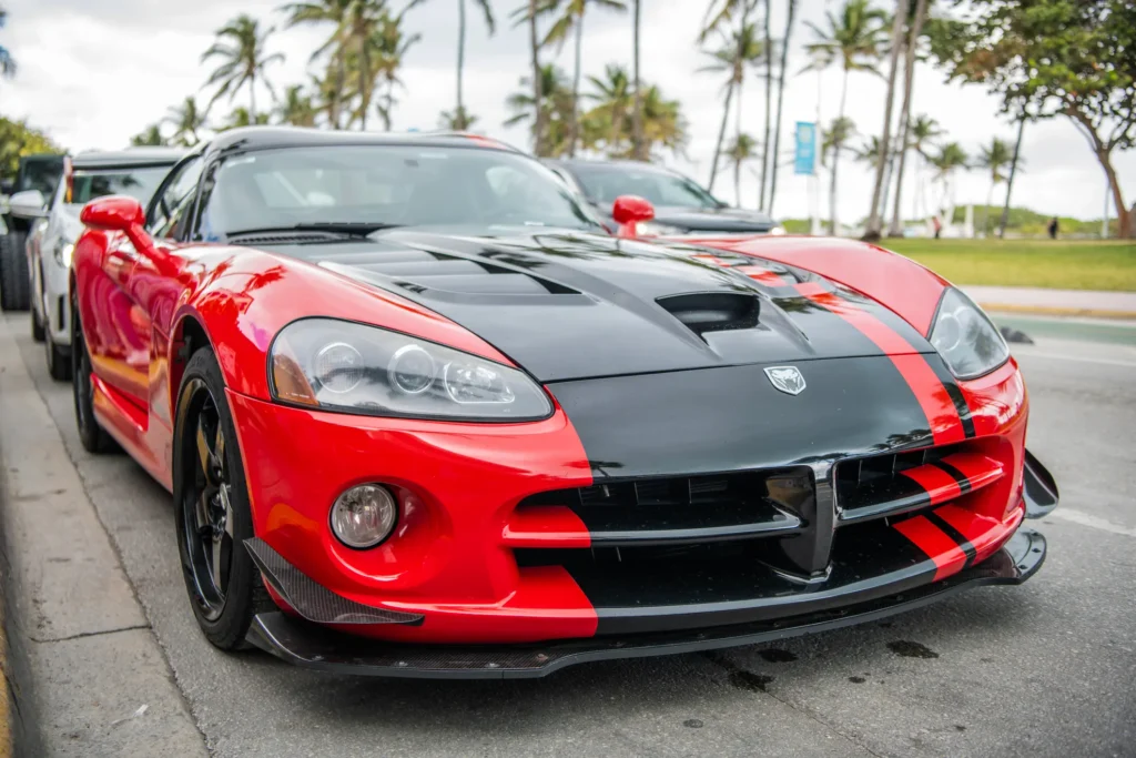 Rote und schwarze Dodge Viper mit Rennstreifen, geparkt unter Palmen für einen Autoankauf‑für‑Export‑Eintrag.